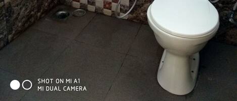 A bathroom with a tiled shower wall, a toilet, and a marble floor.