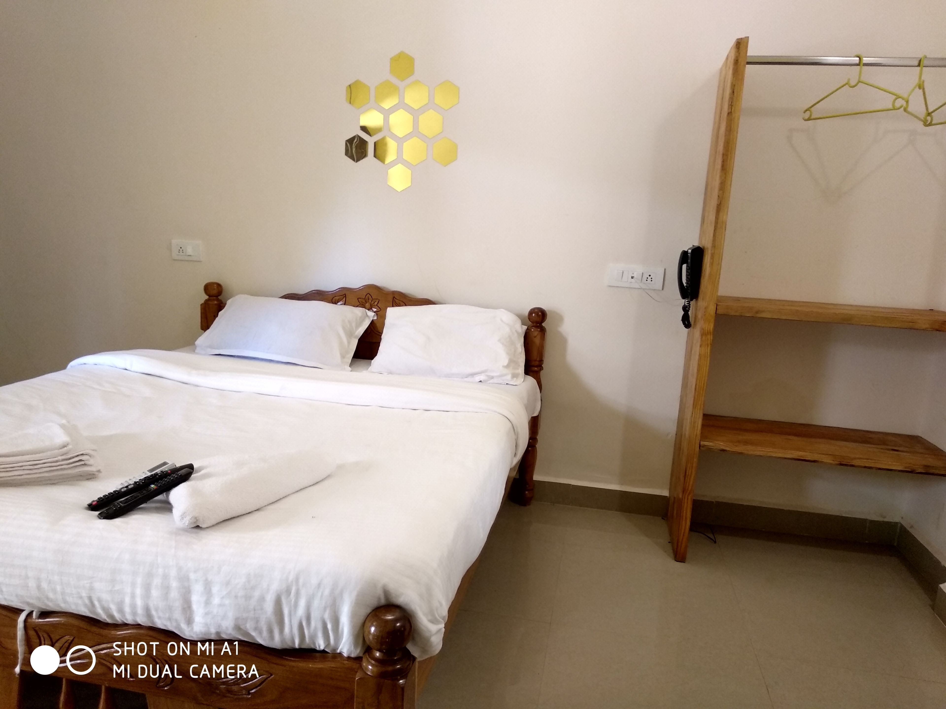 A neatly made bed with white linens and pillows, a wooden headboard, a wall-mounted phone, and a small shelf with hangers.