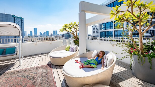 A rooftop terrace with wicker lounge chairs, a view of the city skyline, and potted plants.