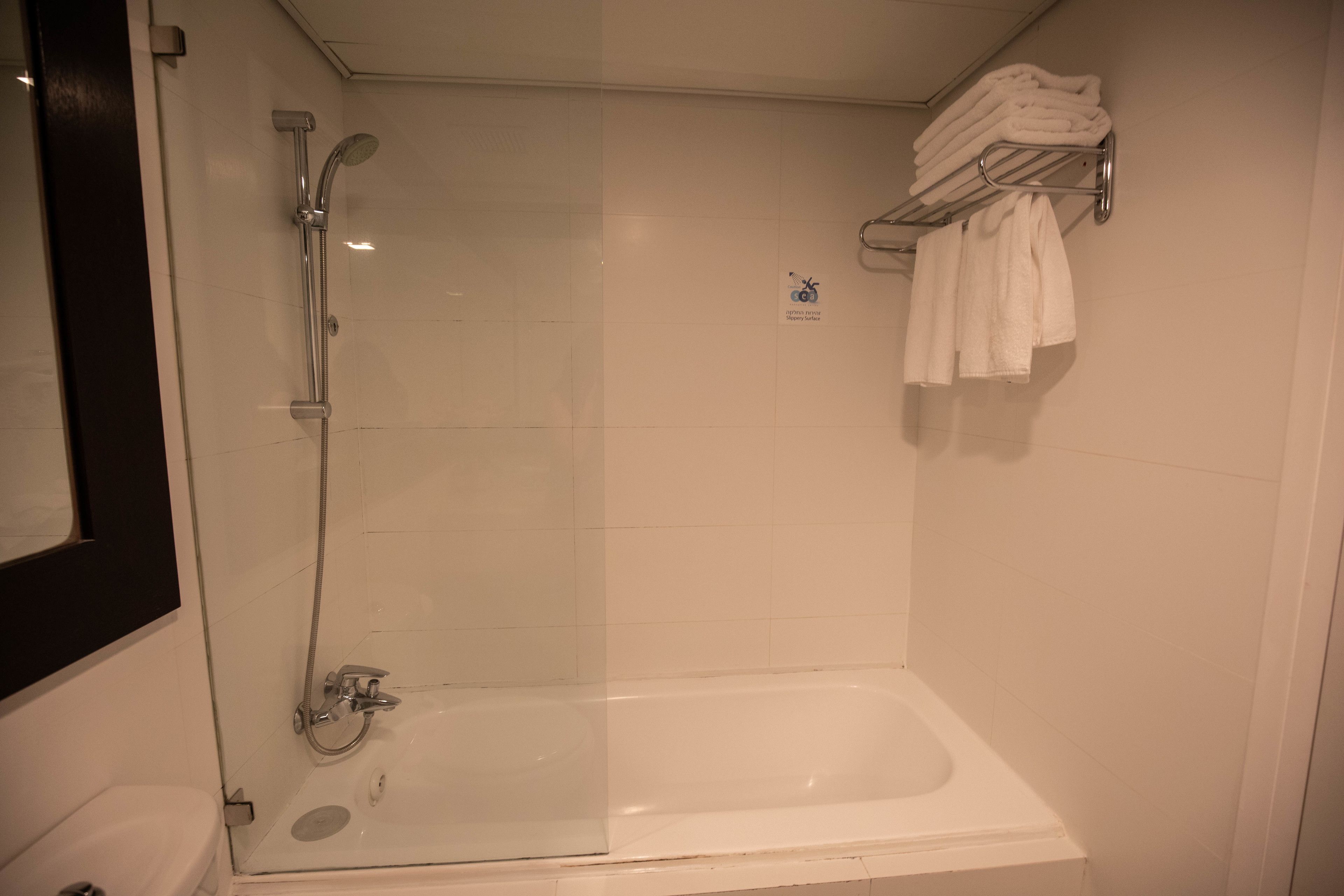 Zona de ducha con mampara de vidrio, bañera y toallero con toallas dobladas.