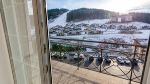 A view from a balcony overlooking a parking area with several cars, a ski slope in the background, and a building with multiple stories. - AmstelSki Hotel (Bukovel)