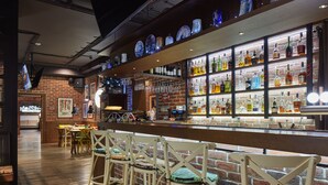 A bar area with wooden bar stools, a brick wall, and shelves of liquor bottles. - AmstelSki Hotel (Bukovel)