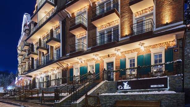 A multi-story building with a beer club sign, outdoor seating, and a staircase leading to the entrance. - AmstelSki Hotel (Bukovel)