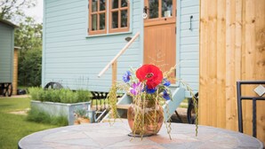 A round stone table with a clear glass vase containing red and blue flowers. - Morndyke Shepherds' Huts (Thirsk)