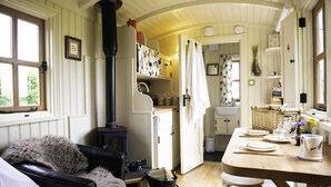 A cozy room with a fireplace, a dining table set for two, and a comfortable sofa. - Morndyke Shepherds' Huts (Thirsk)