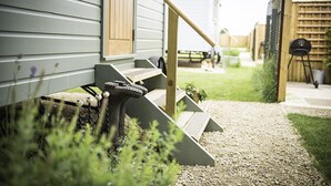A residential property with a wooden staircase leading to a front door, a small porch area, and a garden with a gravel path. - Morndyke Shepherds' Huts (Thirsk)