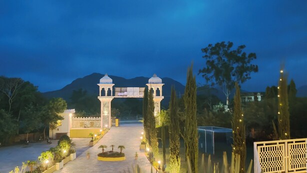 A well-lit entrance with a central archway, surrounded by trees and a mountain in the background. - Alcor Kumbhalgarh – the family getaway (Kumbhalgarh)