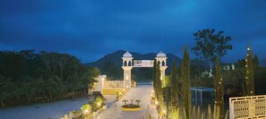 A well-lit entrance with a central archway, surrounded by trees and a mountain in the background. - Alcor Kumbhalgarh – the family getaway (Kumbhalgarh)