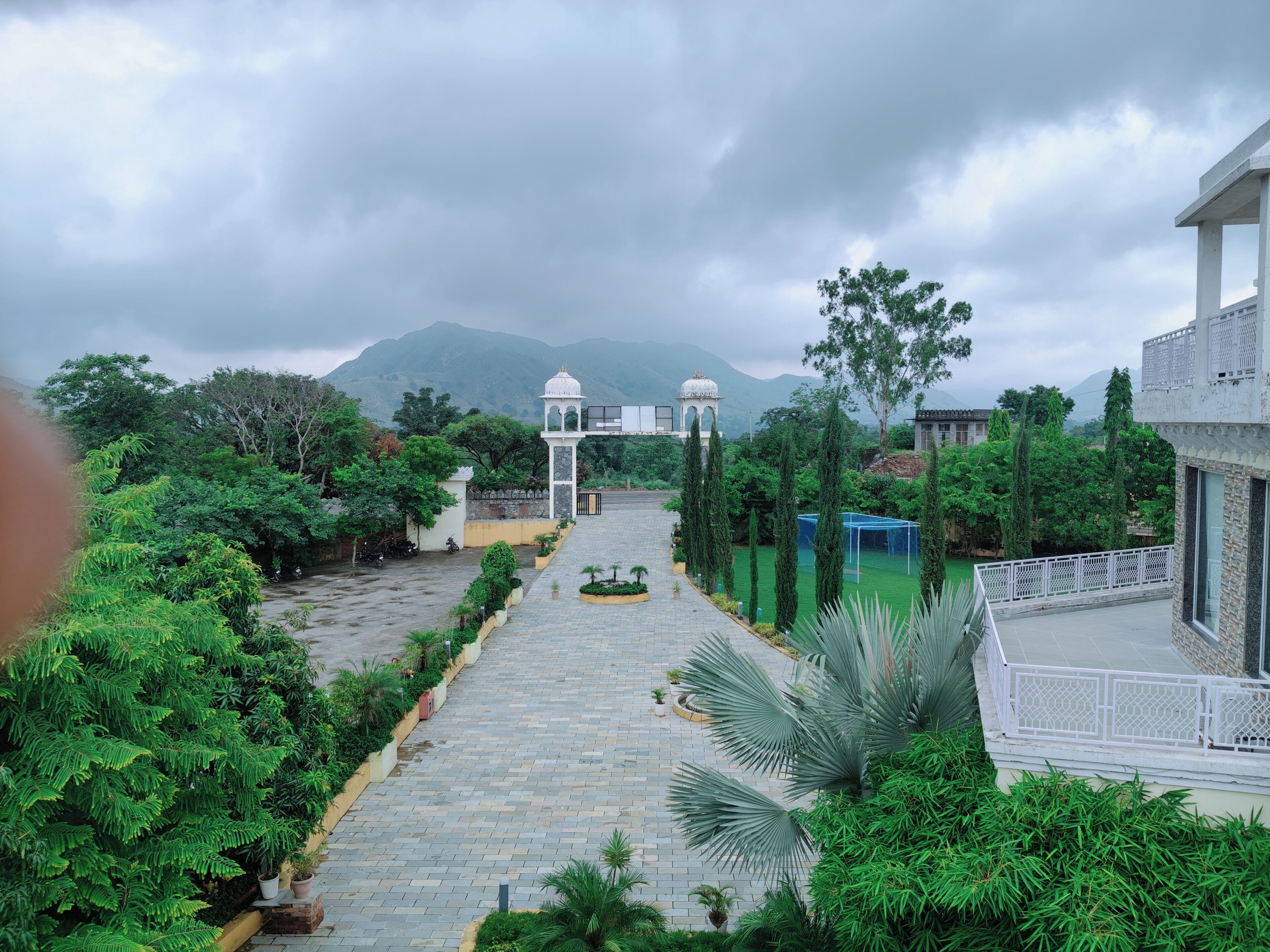 A pathway leading to a white gazebo with a dome, surrounded by lush greenery and a mountainous backdrop.
