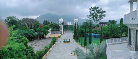 A pathway leading to a white gazebo with a dome, surrounded by lush greenery and a mountainous backdrop.