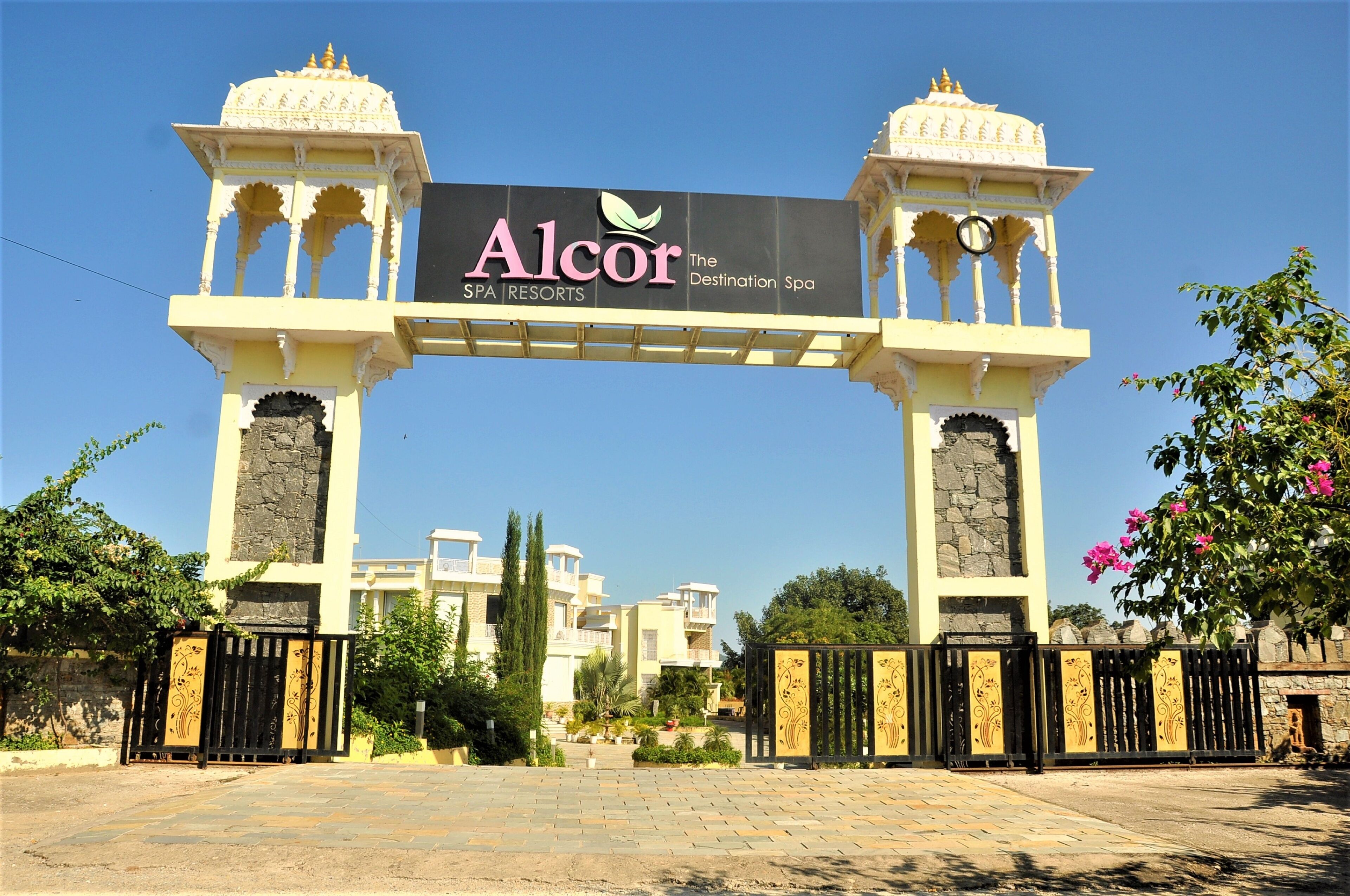 A sign for Alcor Spa Resorts with a traditional architectural style, including a central archway and two towers.