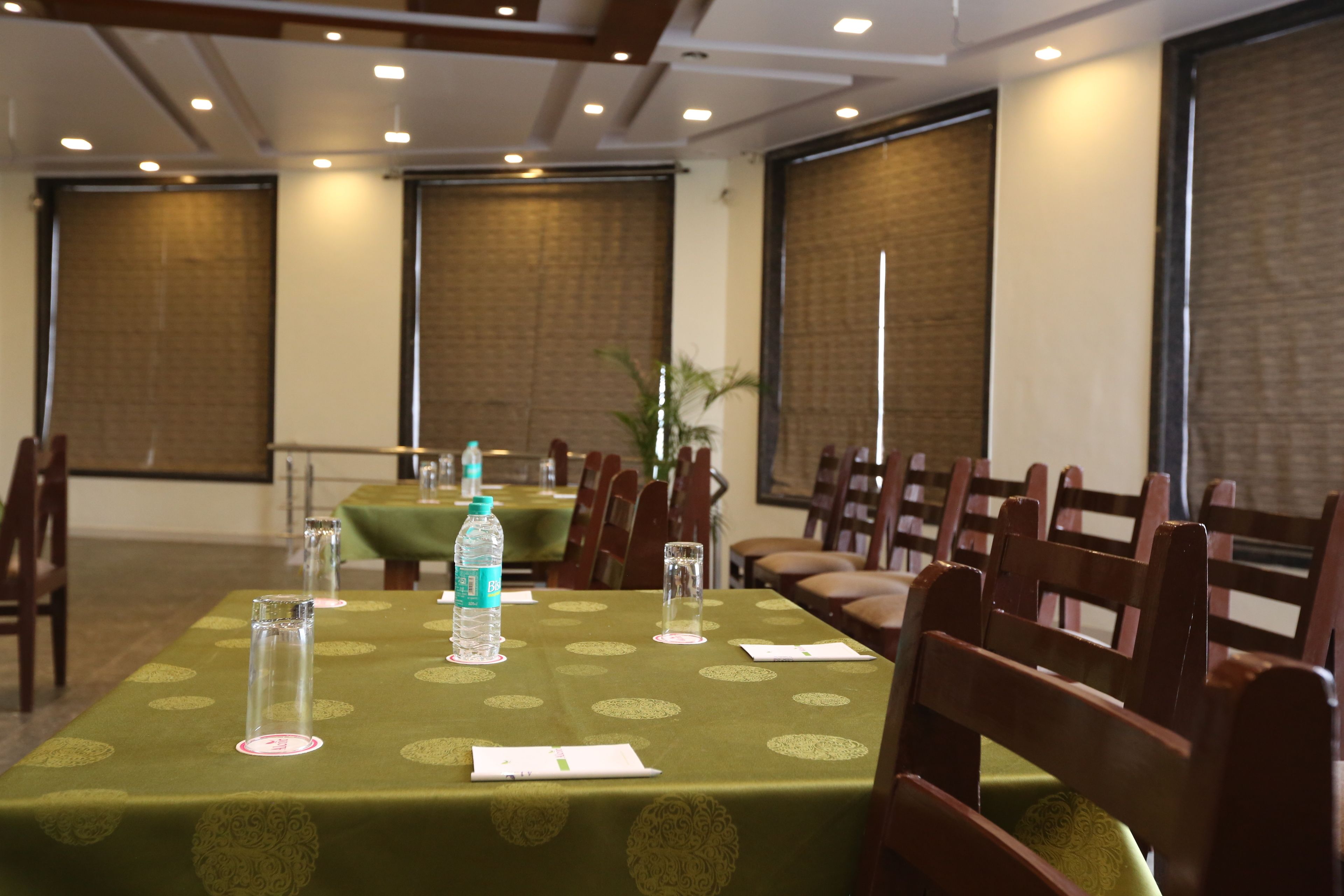 Une salle de conférence avec une table recouverte d’une nappe verte, des chaises, une bouteille d’eau et un verre posés sur la table.