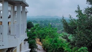 A pathway flanked by lush greenery and a white building with balconies. - Alcor Kumbhalgarh – the family getaway (Kumbhalgarh)
