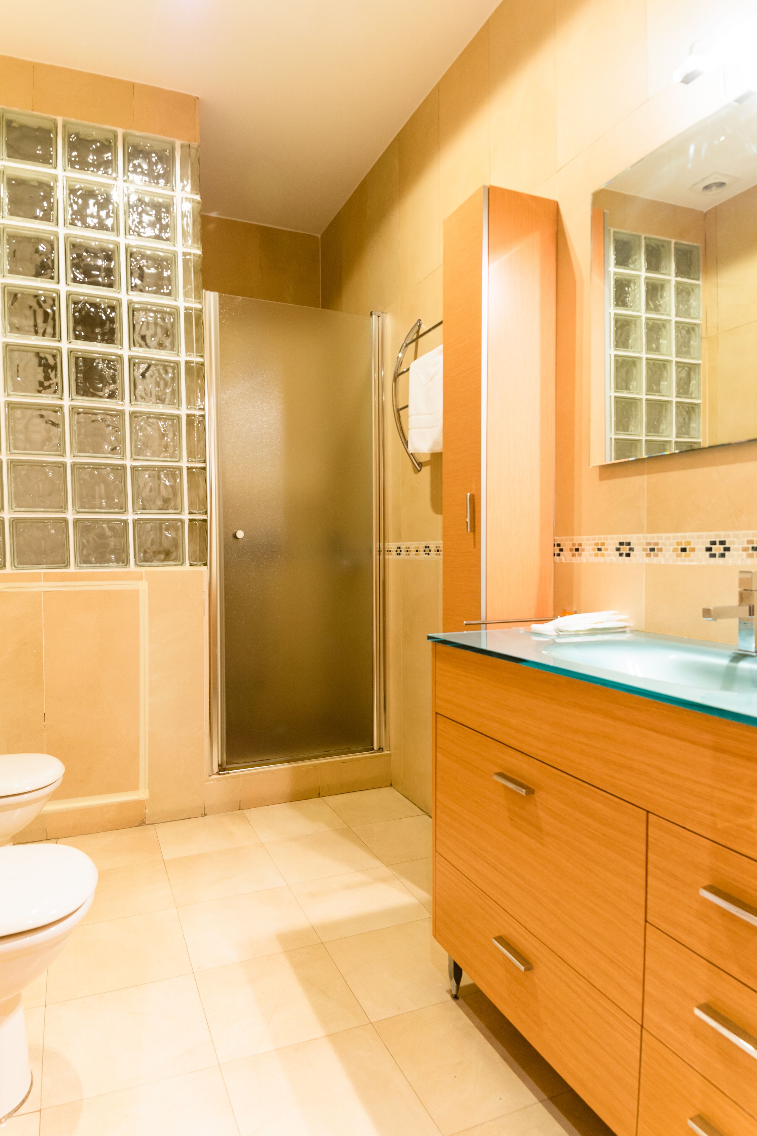 A bathroom with a glass shower enclosure, a toilet, and wooden cabinets.