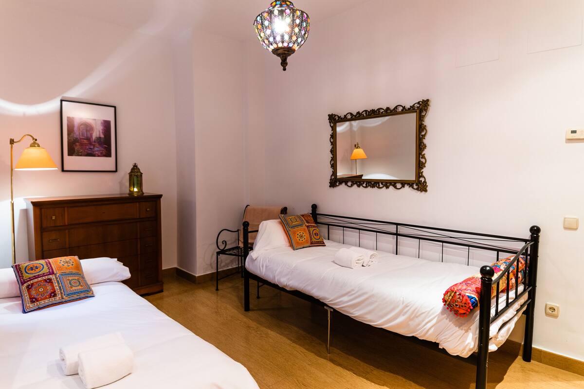 A bedroom with two beds, a wooden dresser, a mirror, and a chandelier.
