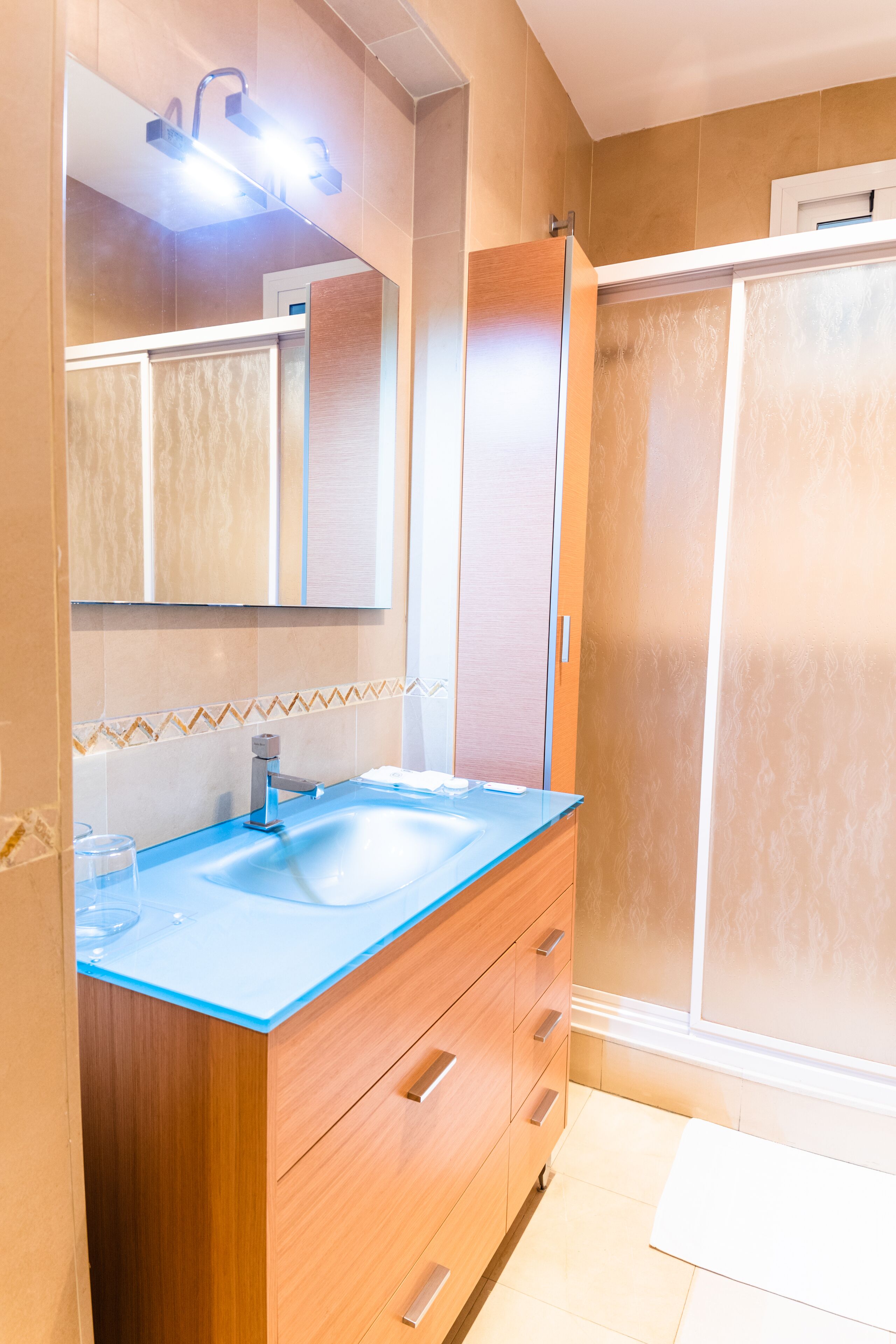 Une salle de bain avec un meuble-lavabo en bois, un lavabo en verre et un espace douche.