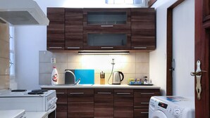 A compact kitchen with wooden cabinets, a built-in stove, a washing machine, and a coffee maker. - Charles Bridge Apartment (Prague)
