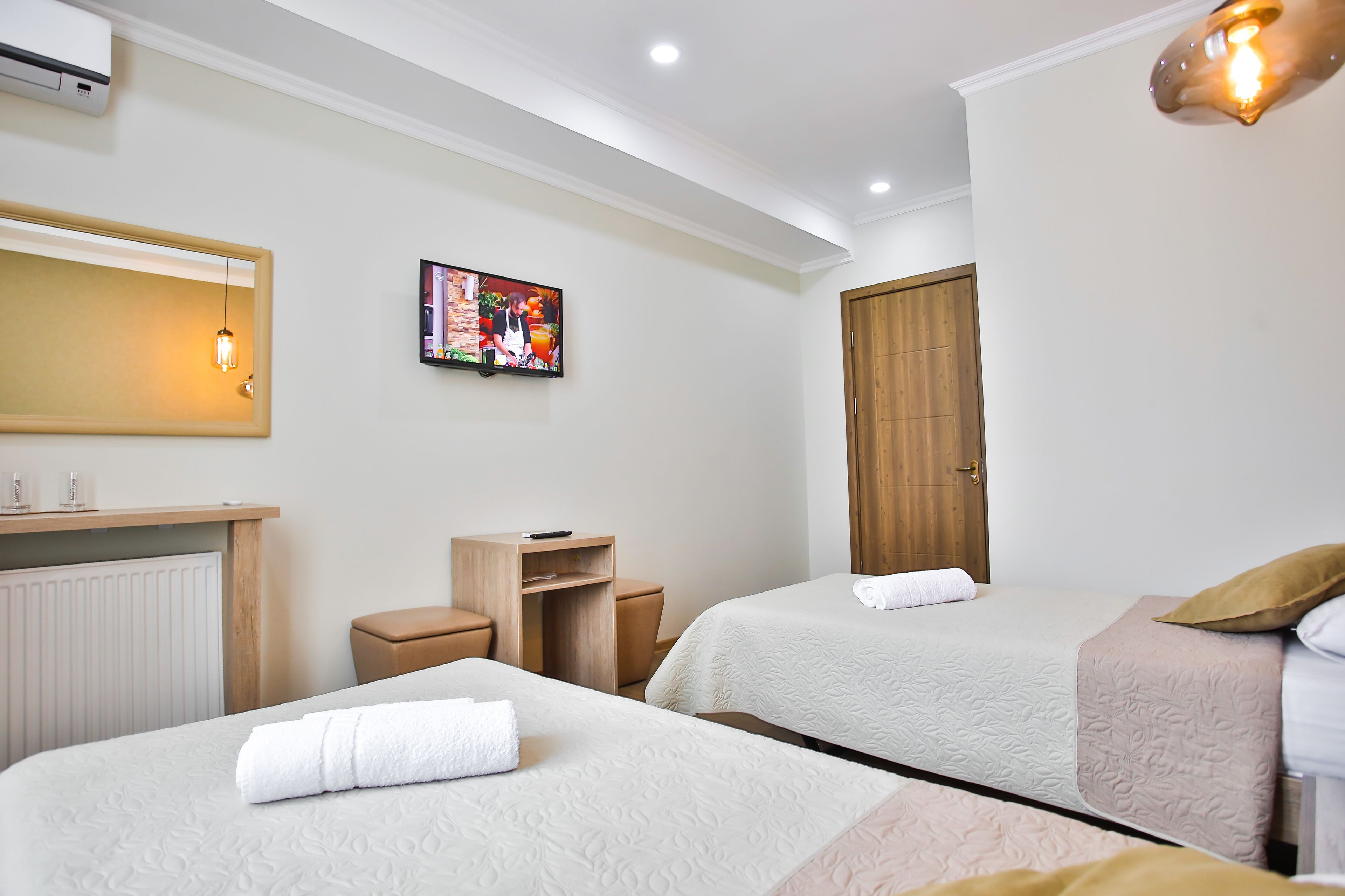 A hotel room with two beds, a TV, a wooden wardrobe, a desk, and a radiator.