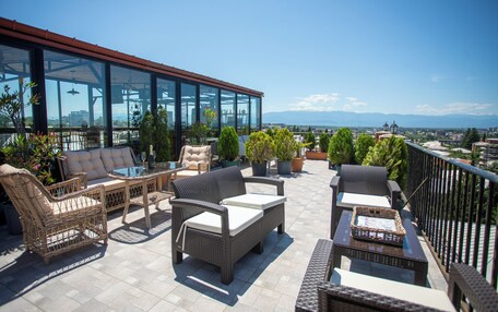 A rooftop terrace with wicker furniture, potted plants, and a glass-enclosed area.