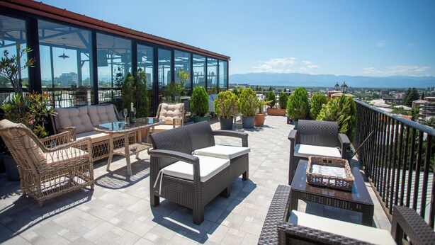 Une terrasse sur le toit, aménagée avec des meubles en osier, des plantes en pot et un espace clos par des parois de verre.