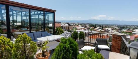 A rooftop terrace with outdoor seating, potted plants, and a glass-enclosed structure.