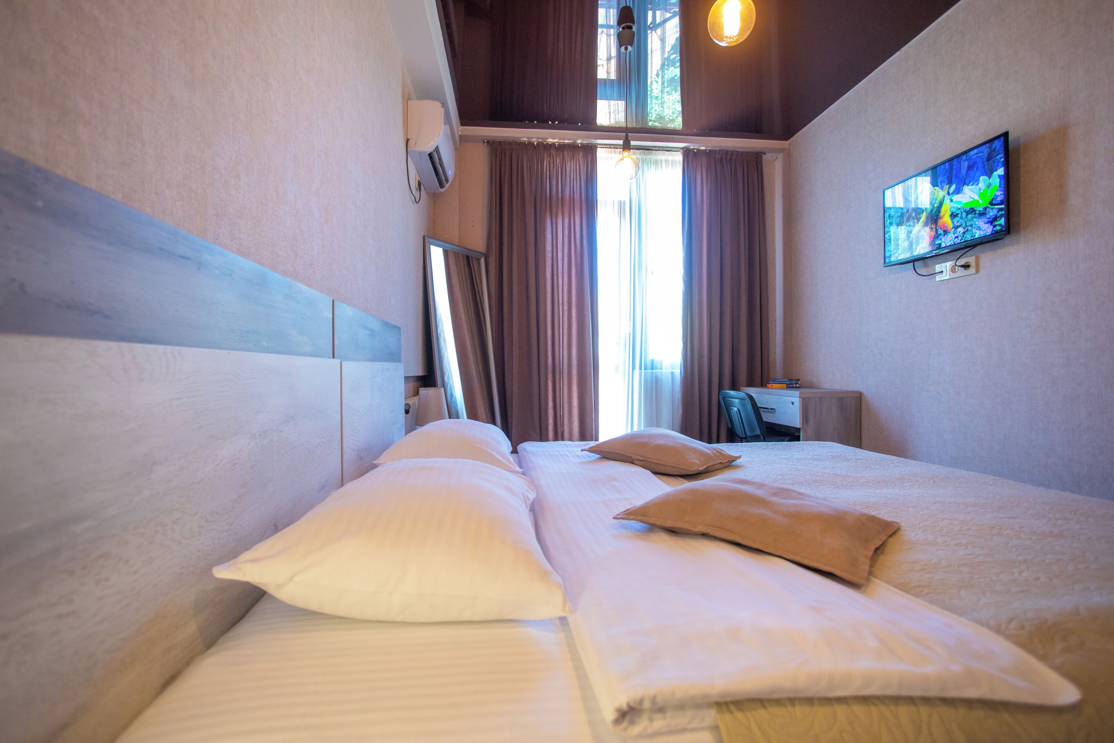 Habitación de hotel con cama, almohadas, televisión en la pared y ventana con cortinas.