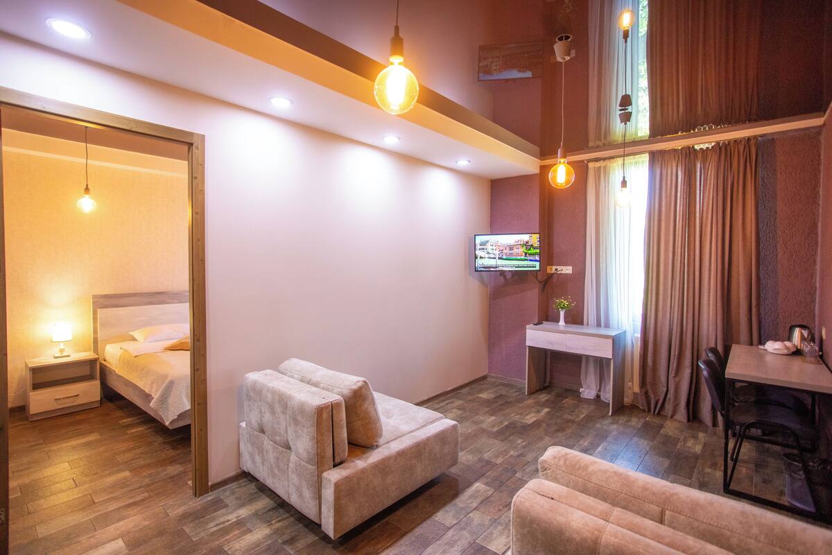 A modern hotel room with a sofa, a small table, a TV, and a bed.