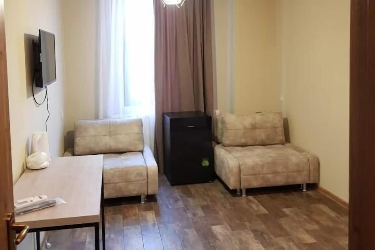 A small, furnished room with a sofa, a table, and a TV mounted on the wall.