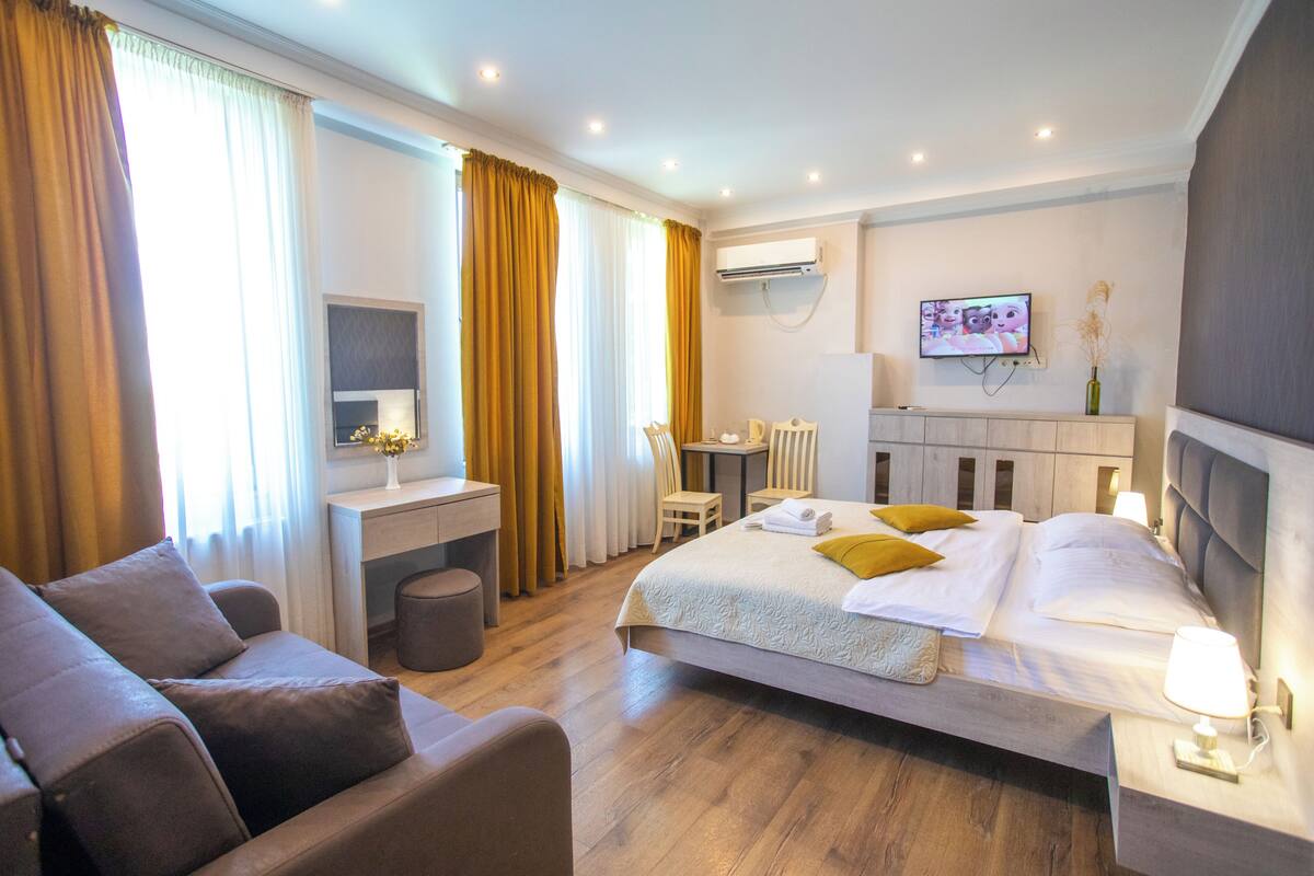 A hotel room with a bed, a desk, a chair, a TV, and a lamp.