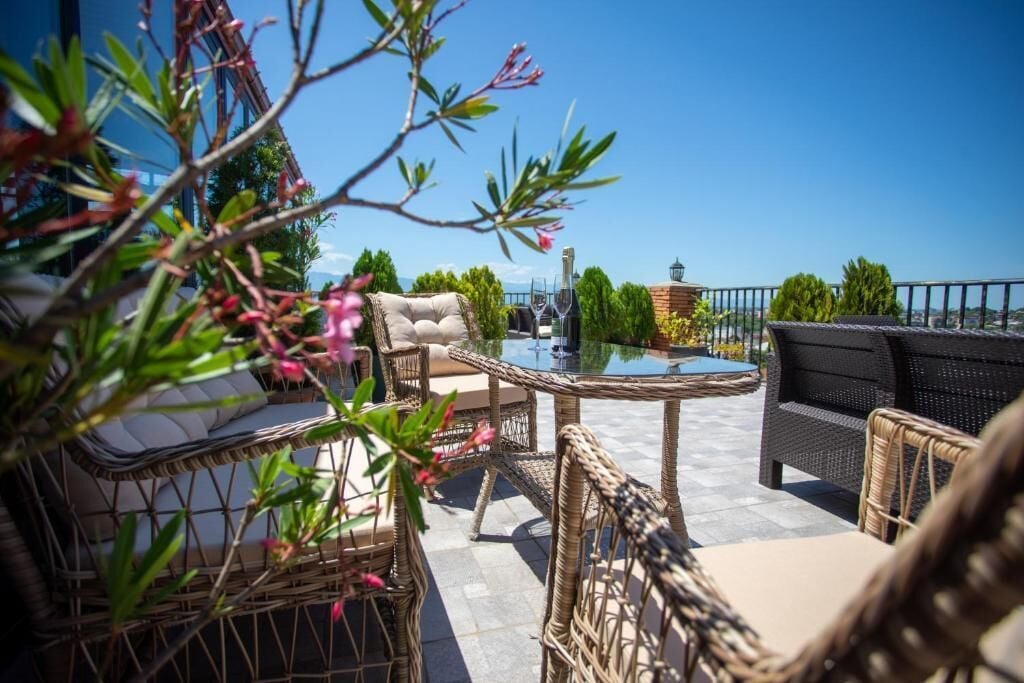 An outdoor patio area with wicker furniture, a glass table, and a view of the sea.