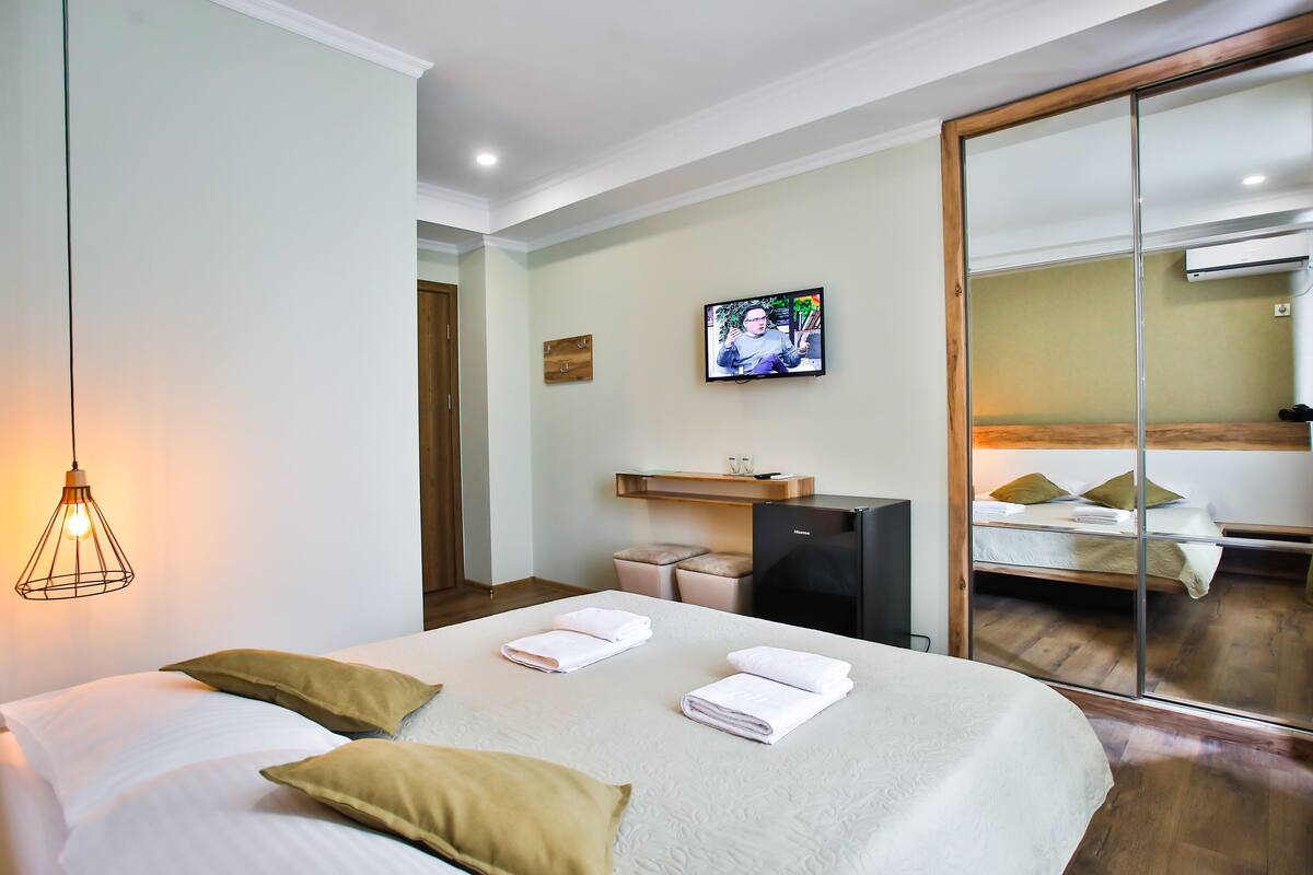 A hotel room with a bed, a TV, a desk, and a mirror.