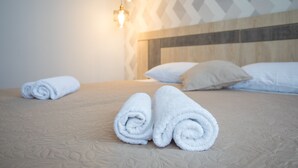 Un lit bien fait, avec des serviettes blanches pliées en rouleaux, une tête de lit en bois et un mur orné d’un motif.