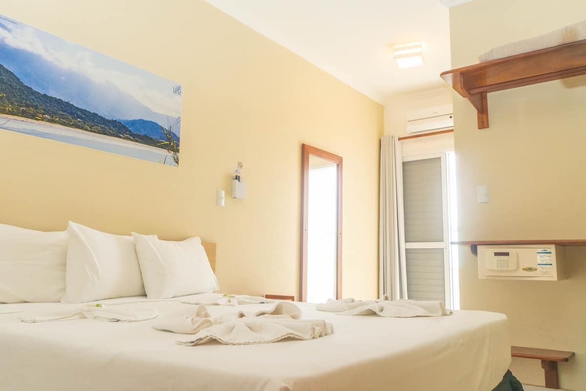 A hotel room with a bed, a wall-mounted air conditioner, and a window with curtains.