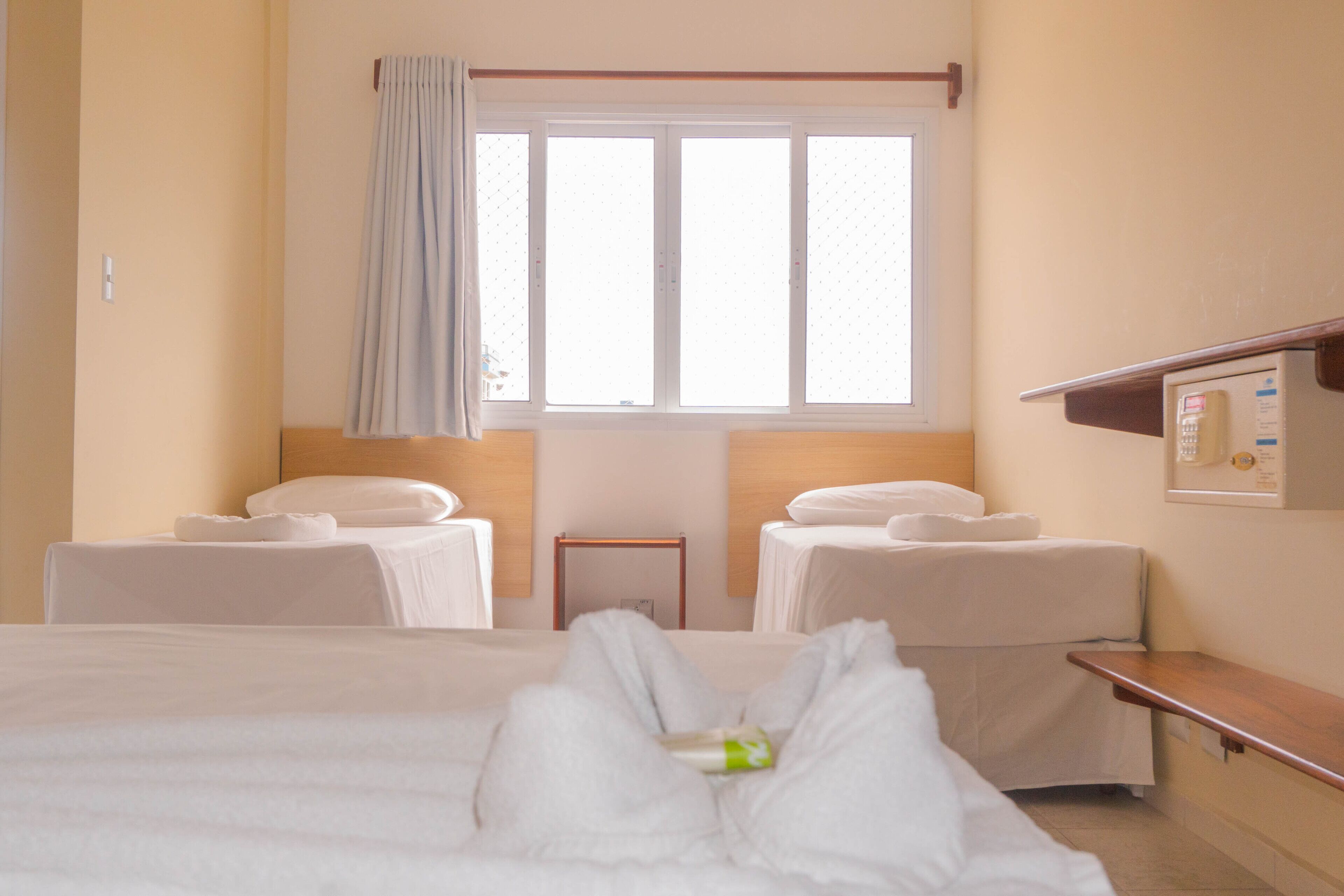 A hotel room with a large bed, two bedside tables, a window with curtains, and a wall-mounted control panel.