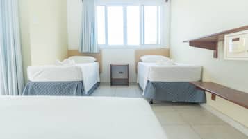 Una habitación de hotel con dos camas, una mesita, una mesita de noche, una ventana con cortinas y un teléfono en la pared.