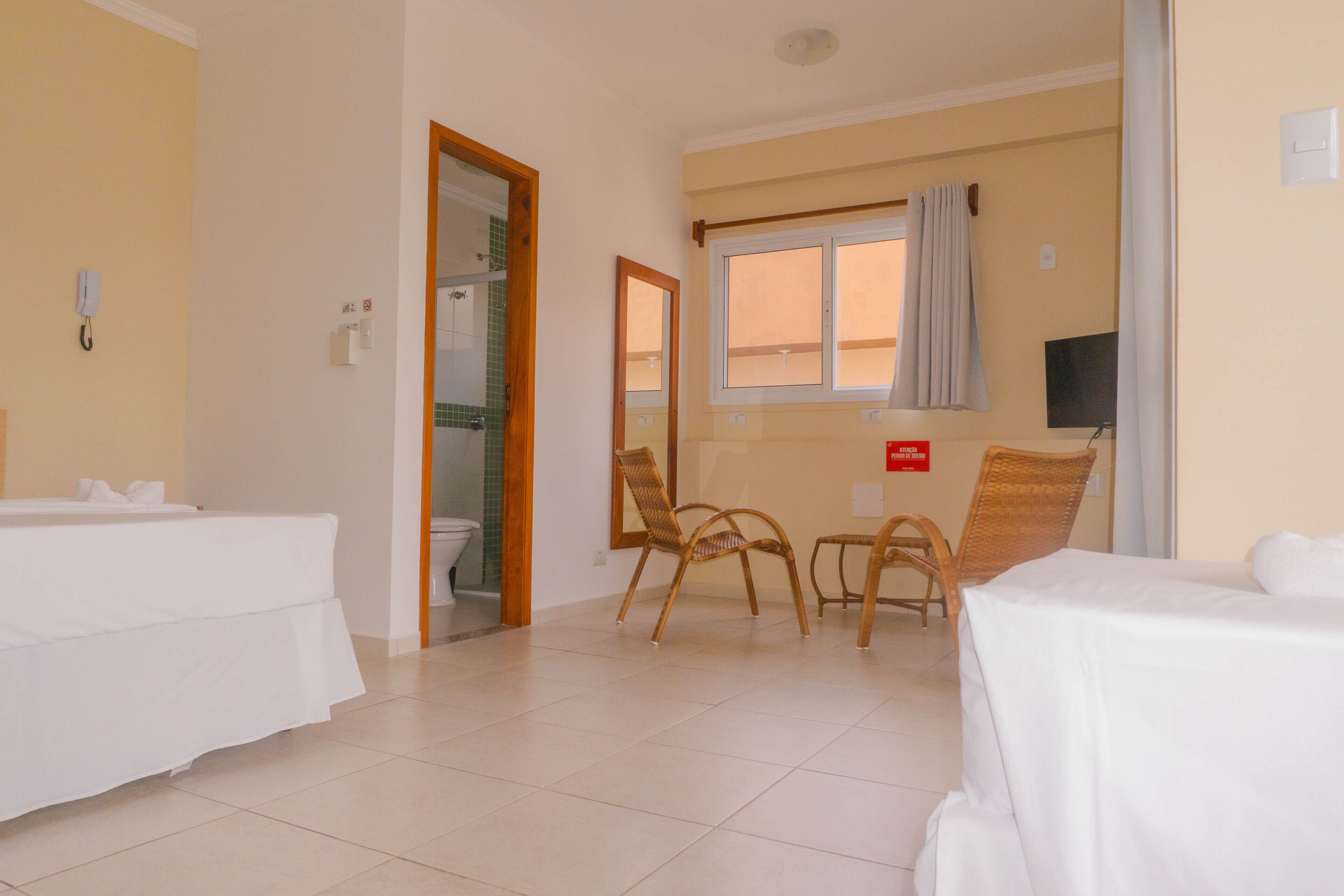 A hotel room with two beds, a bathroom, a television, and a window with curtains.