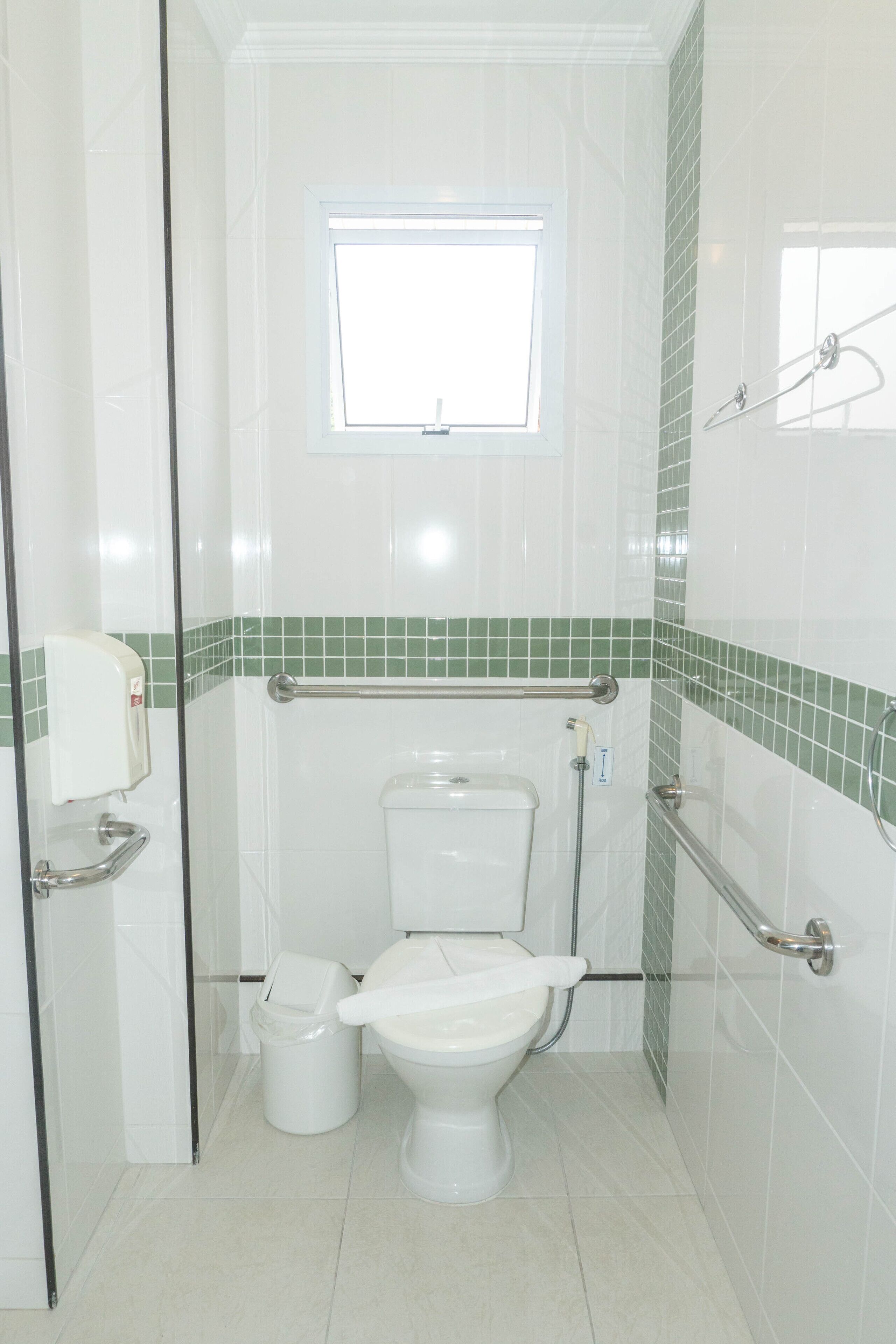 Un baño con inodoro, secador de manos, ventana y cabina de ducha de vidrio.