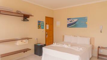 Una habitación de hotel con una cama, un estante de madera, un cuadro de un barco y una puerta.
