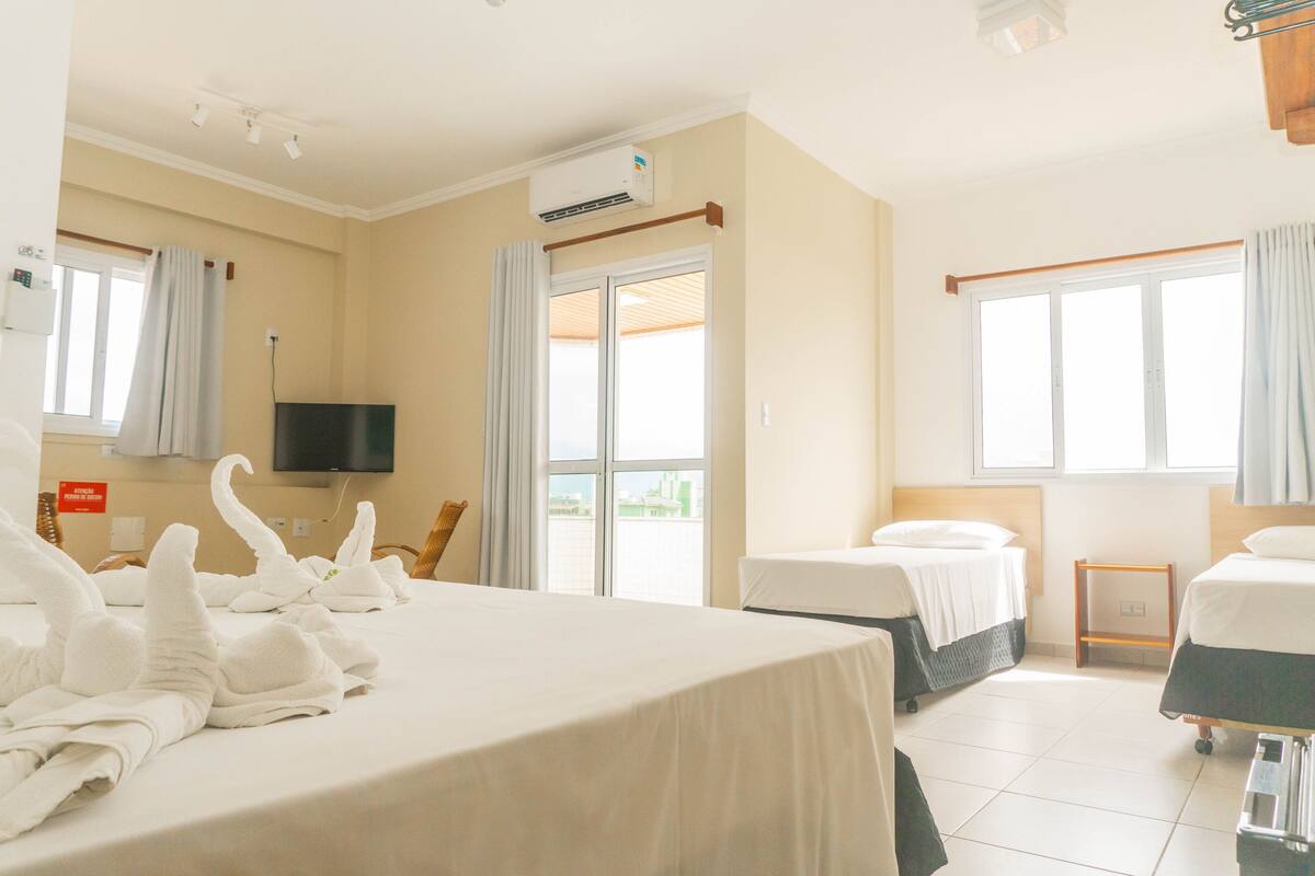 A hotel room with two beds, a television, an air conditioning unit, and a window with curtains.