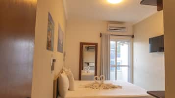 Habitación de hotel con cama, almohadas, televisión de pantalla plana, aire acondicionado y una ventana con cortinas.