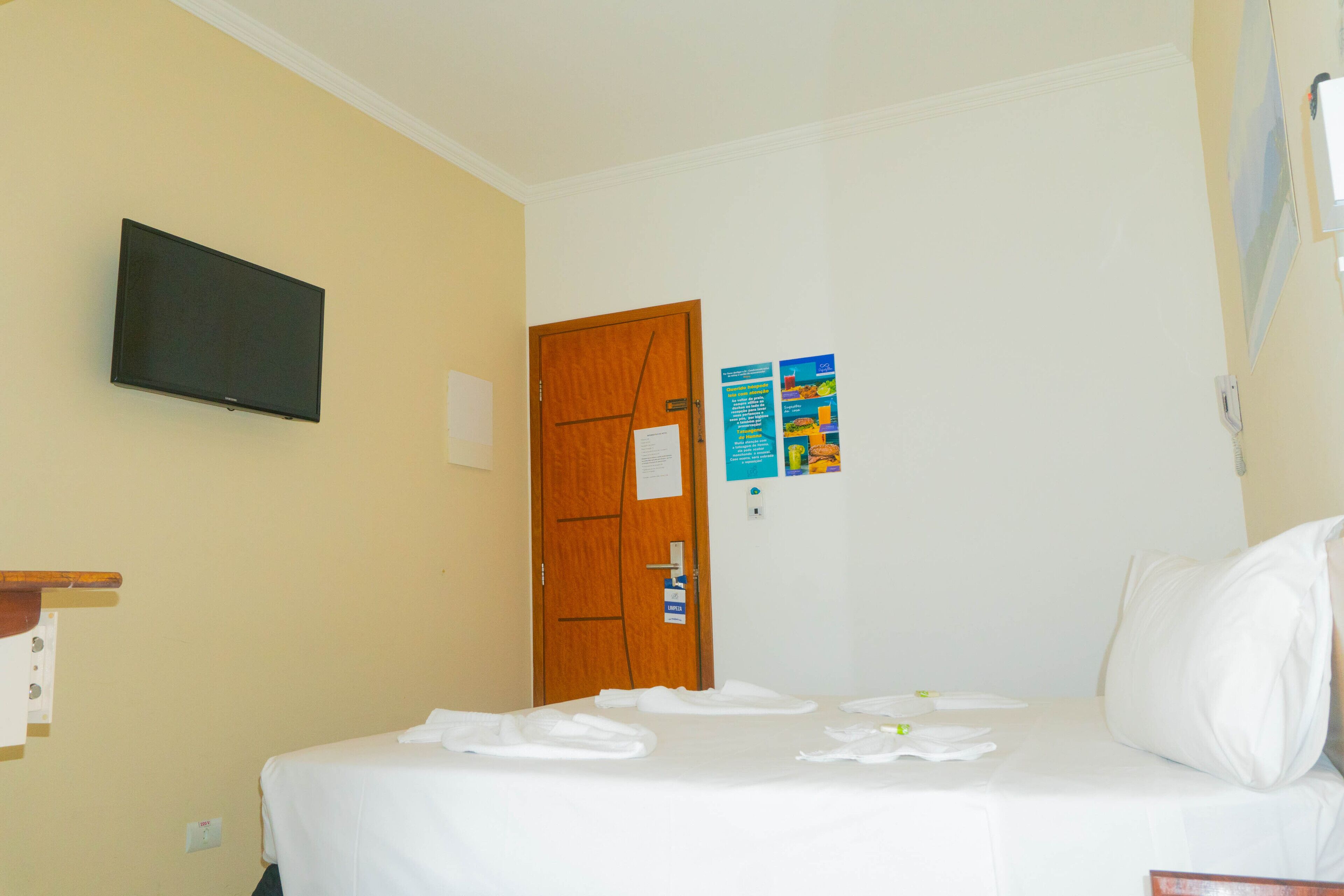 Una camera d'albergo con un letto, una televisione montata a parete e una porta con un cartello.
