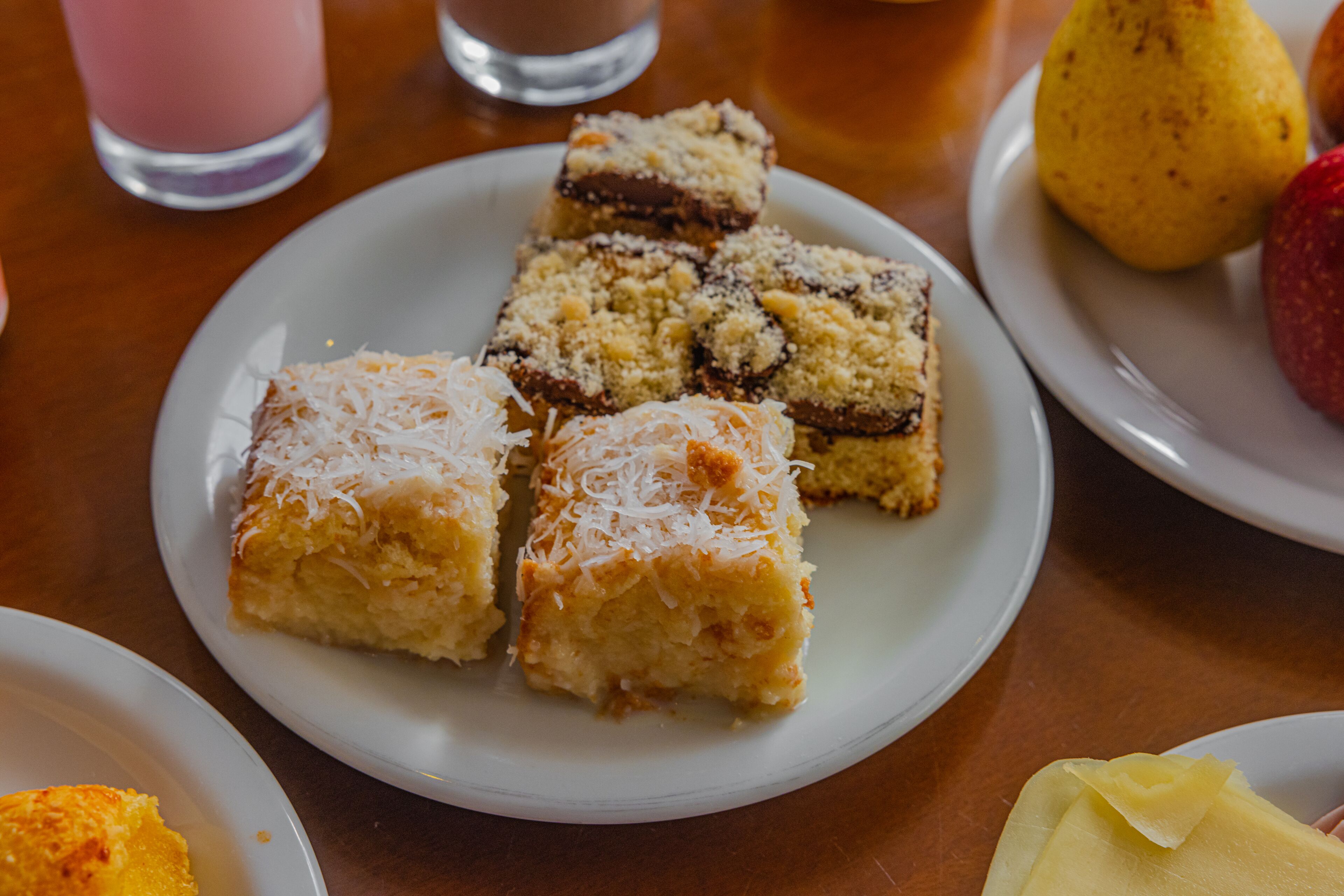 Een bord met diverse vierkante desserts, een glas roze drank en een peer op een tafel.