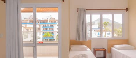 Habitación de hotel con dos camas, una ventana con cortinas, vistas a edificios y un equipo de aire acondicionado.