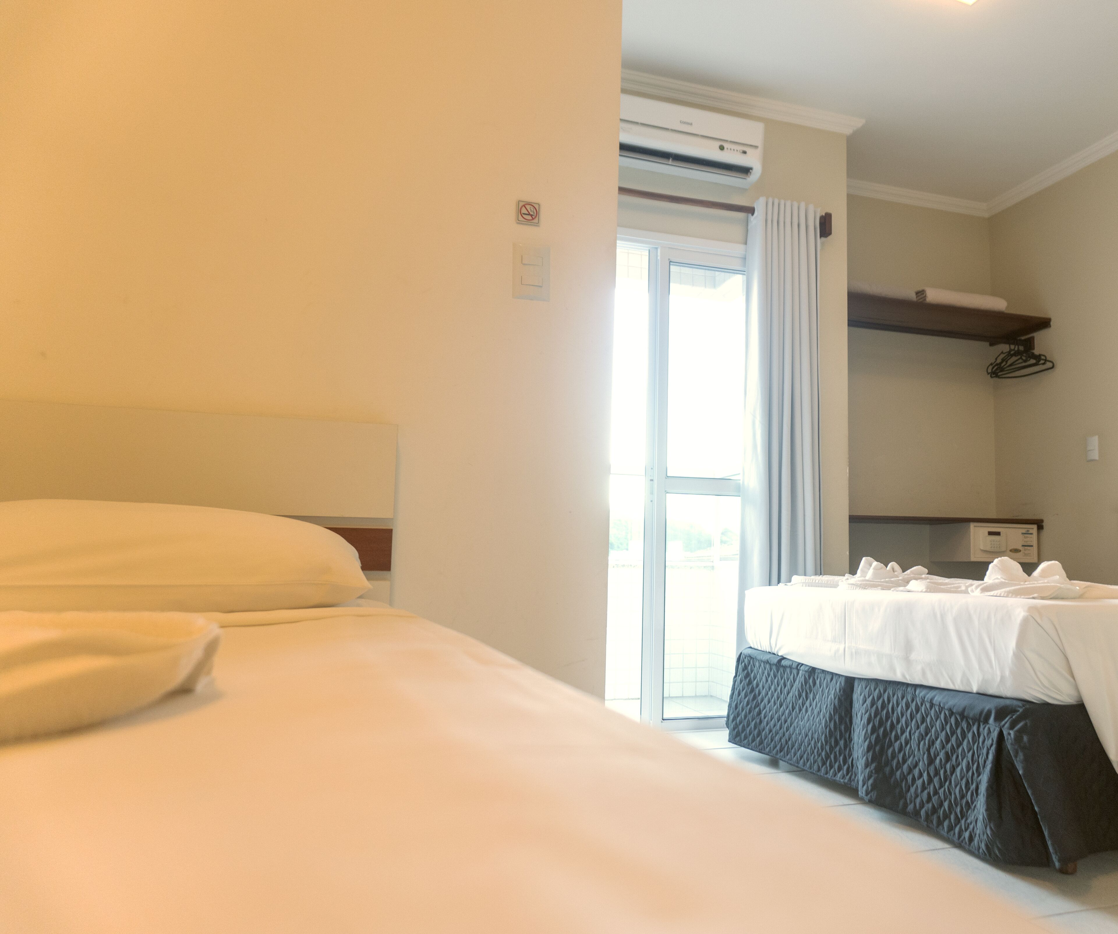 Habitación de hotel con una cama grande, una cama más pequeña, un escritorio y una ventana con cortinas.