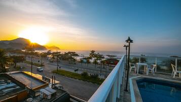 Vista da piscina com pôr do sol, uma rua e uma montanha ao fundo.