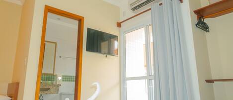 Habitación de hotel con cama, baño visible a través de una puerta abierta, televisor montado y unidad de aire acondicionado.