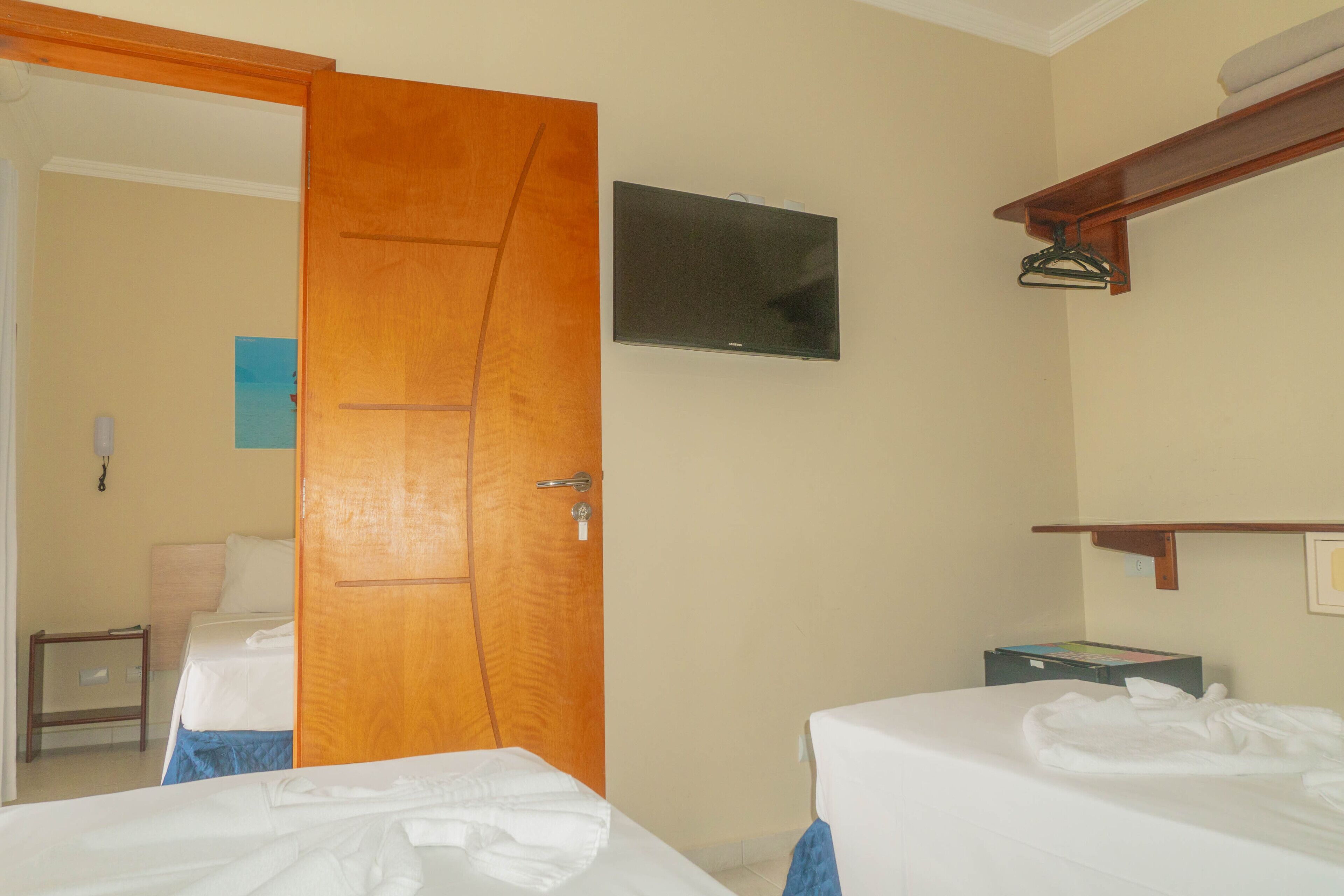 Una habitación de hotel con dos camas, un televisor montado en la pared, una puerta de madera y una mesita.