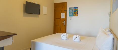 Una habitación de hotel con una cama, un televisor en la pared, una puerta de madera y un tablón de anuncios.