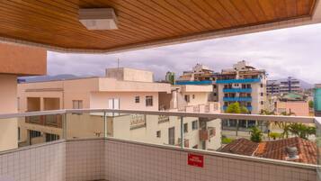Un balcón con suelo de baldosas y techo de madera, con vistas a un paisaje urbano que incluye edificios y montañas al fondo.