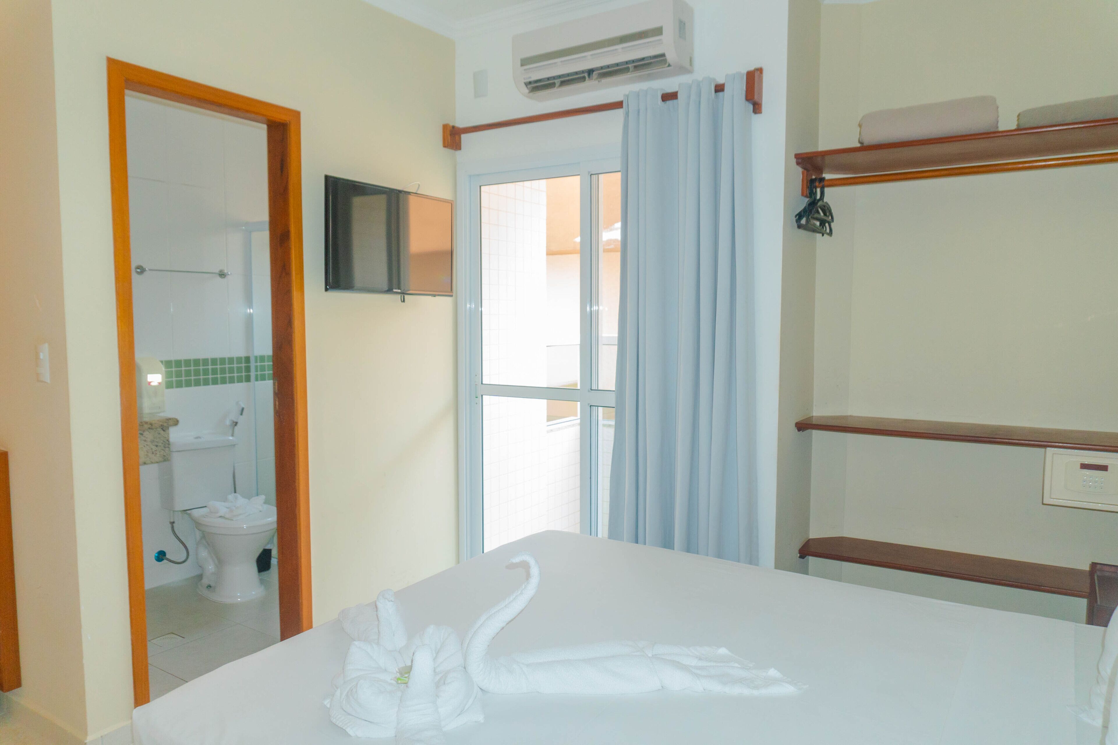 Camera d'albergo con un letto, un bagno con il water, una doccia, una TV montata a parete e una finestra con tende.